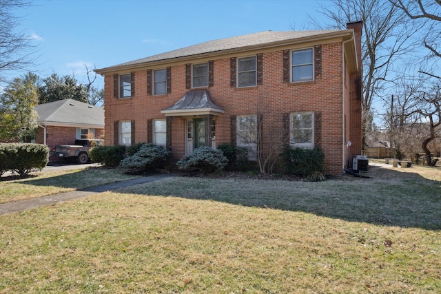 colonial house featuring brick siding, a chimney, and a front yard