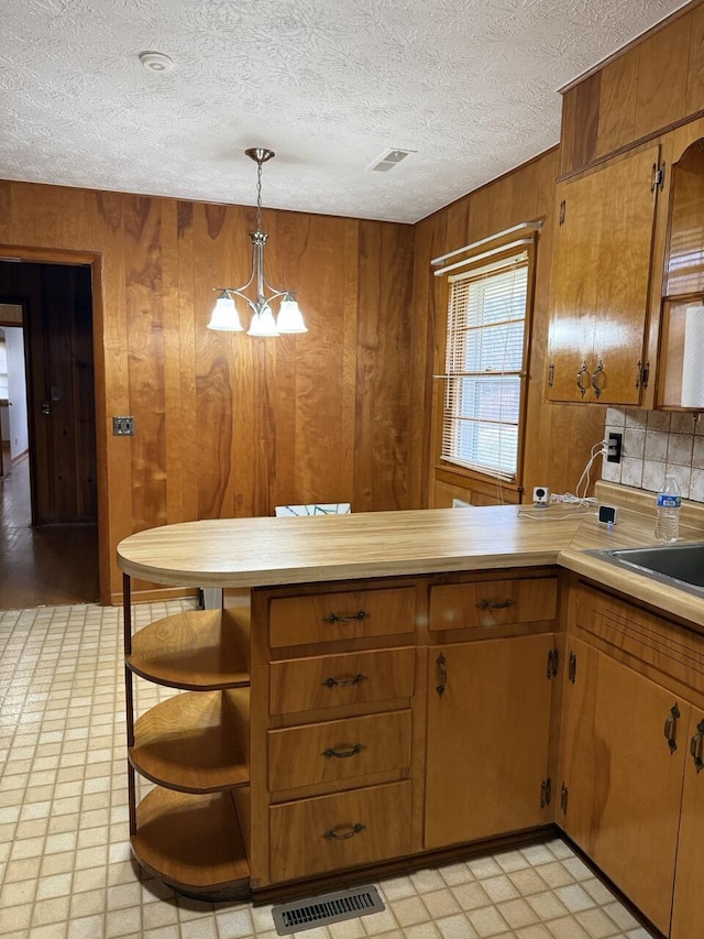 kitchen with wooden walls, decorative light fixtures, sink, a chandelier, and a textured ceiling