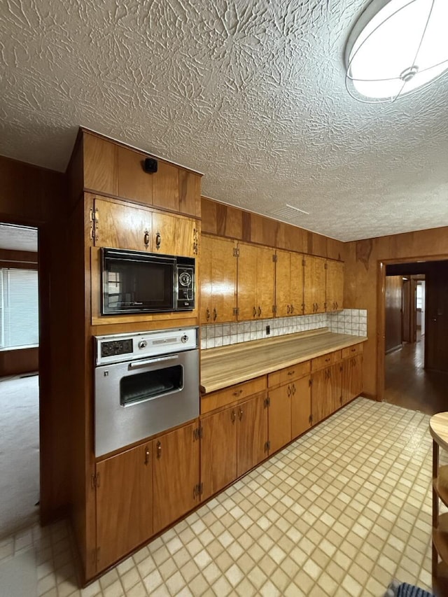 kitchen featuring oven, a textured ceiling, and wood walls