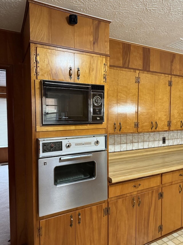 kitchen with decorative backsplash, stainless steel oven, black microwave, and a textured ceiling