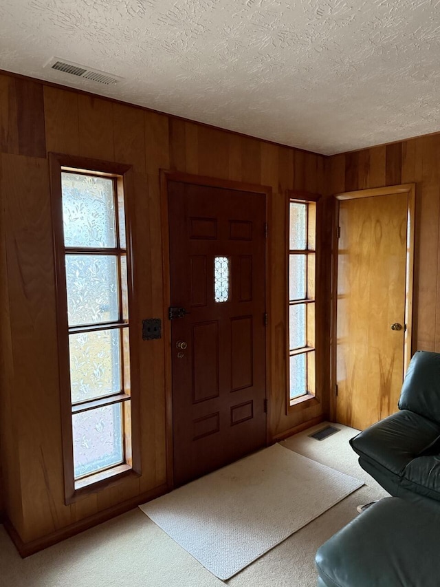 carpeted foyer with wooden walls and a textured ceiling