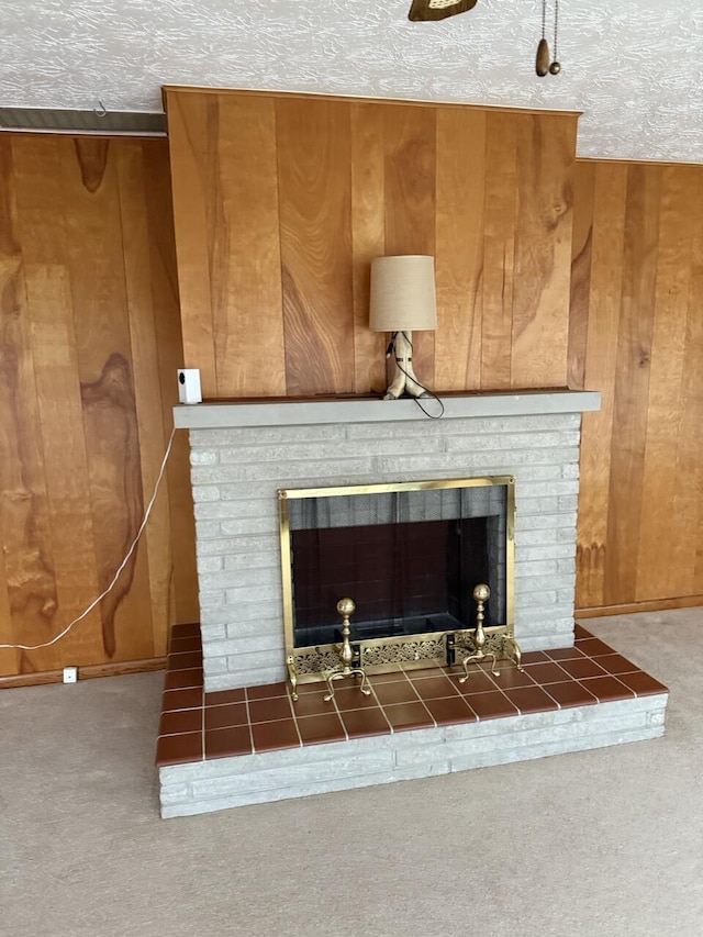 interior details featuring a brick fireplace, wooden walls, a textured ceiling, and carpet flooring