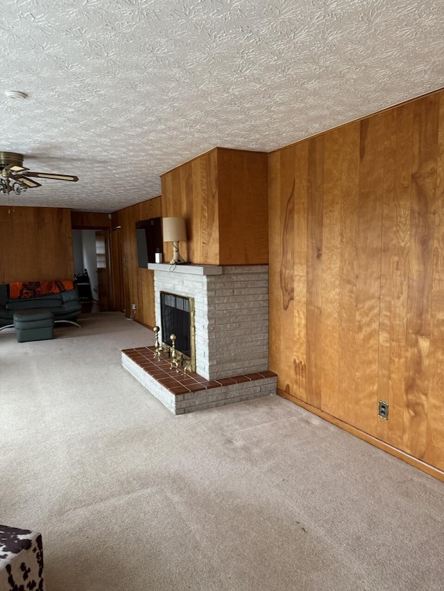 unfurnished living room with ceiling fan, carpet flooring, a textured ceiling, a brick fireplace, and wood walls