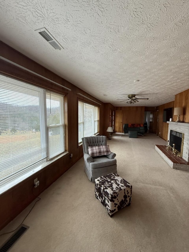 carpeted living room with ceiling fan, a brick fireplace, a textured ceiling, and wooden walls