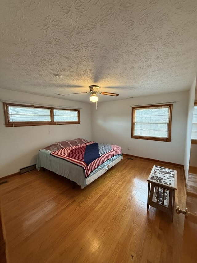 bedroom with hardwood / wood-style floors, a textured ceiling, ceiling fan, and baseboard heating