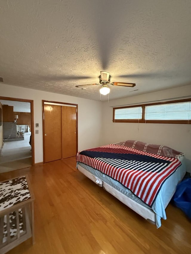 bedroom featuring hardwood / wood-style floors, a textured ceiling, ceiling fan, and a closet