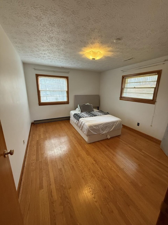 unfurnished bedroom featuring multiple windows, hardwood / wood-style floors, a textured ceiling, and baseboard heating