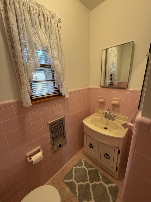 bathroom featuring heating unit, vanity, toilet, and tile walls