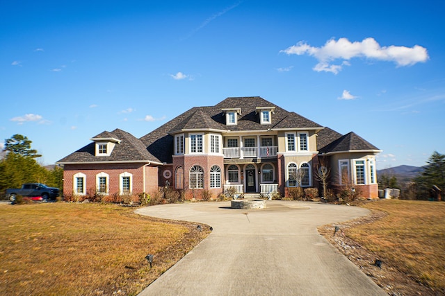 view of front facade with a front yard, concrete driveway, brick siding, and a balcony