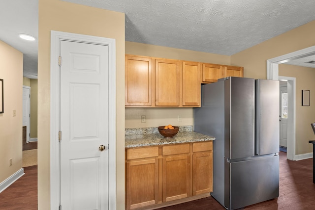 kitchen featuring light stone countertops, a textured ceiling, stainless steel fridge, and dark hardwood / wood-style flooring