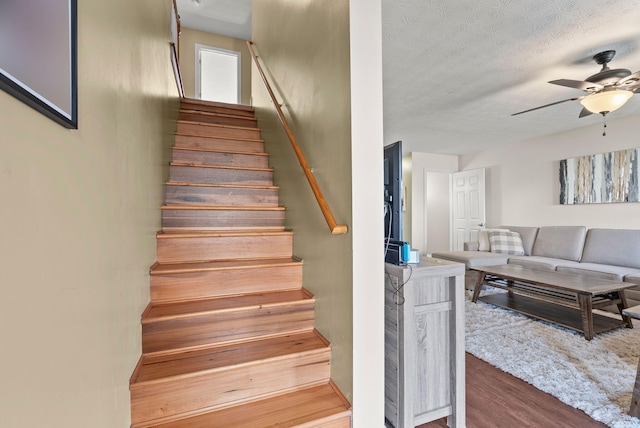 stairway with hardwood / wood-style floors, a textured ceiling, and ceiling fan