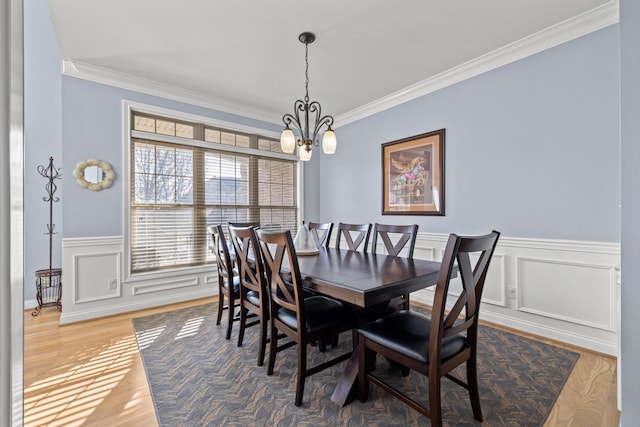 dining area with an inviting chandelier, ornamental molding, a decorative wall, and wood finished floors