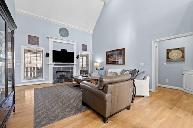 living room featuring a fireplace, light wood finished floors, ornamental molding, high vaulted ceiling, and baseboards