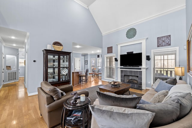 living room featuring crown molding, a fireplace, visible vents, light wood-style flooring, and high vaulted ceiling