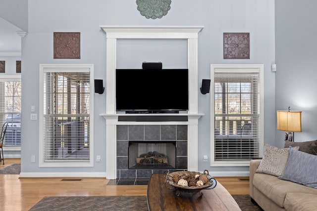 living room featuring baseboards, a tiled fireplace, visible vents, and wood finished floors