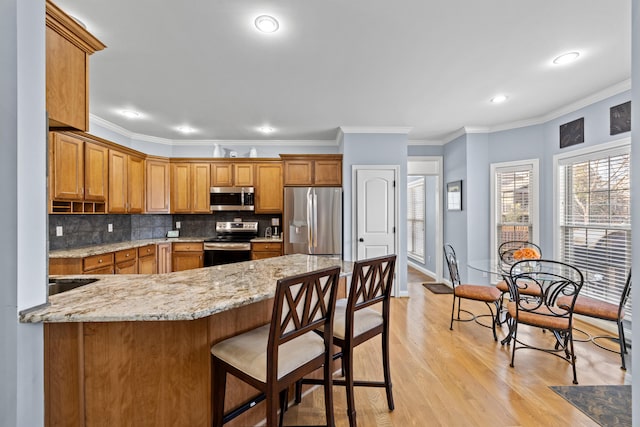 kitchen featuring light wood finished floors, tasteful backsplash, appliances with stainless steel finishes, brown cabinets, and light stone counters