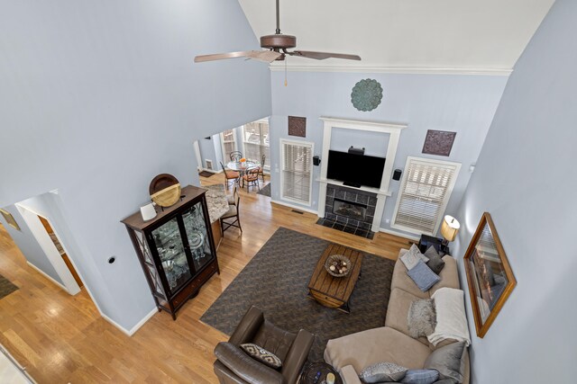 living room featuring baseboards, a tiled fireplace, a towering ceiling, ceiling fan, and light wood-type flooring