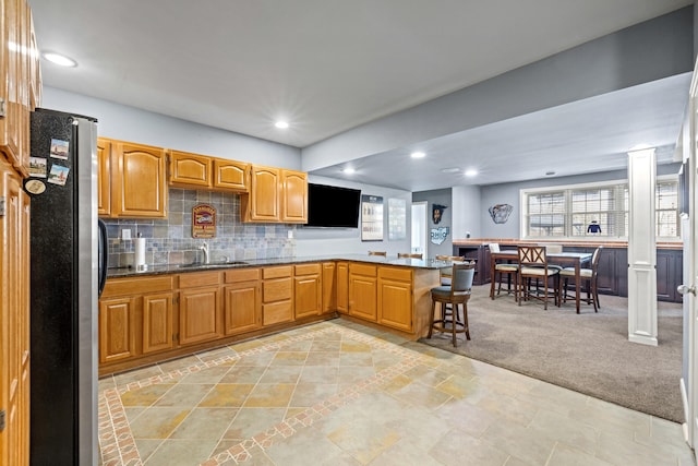 kitchen with brown cabinetry, freestanding refrigerator, a sink, a peninsula, and ornate columns