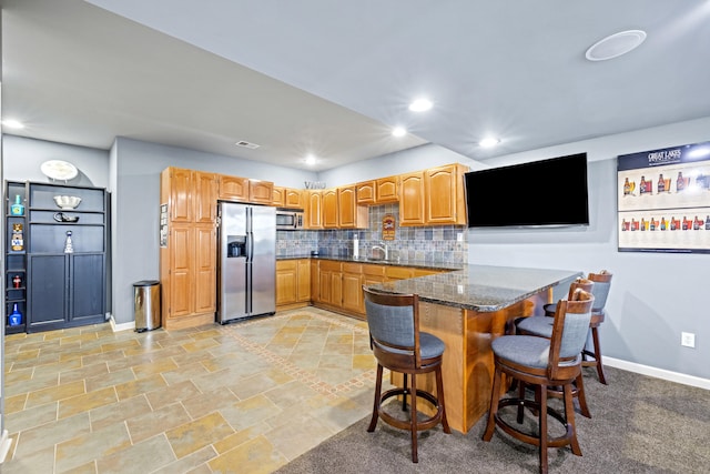 kitchen with stainless steel appliances, a peninsula, tasteful backsplash, dark stone countertops, and a kitchen bar