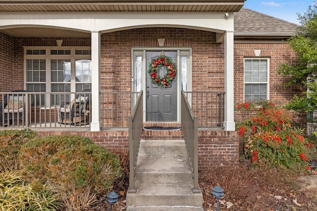 entrance to property featuring roof with shingles and brick siding