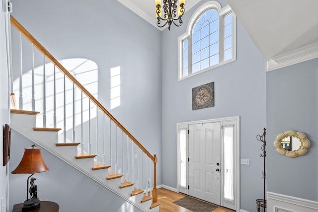 entrance foyer with a towering ceiling, stairway, ornamental molding, light wood-type flooring, and a chandelier