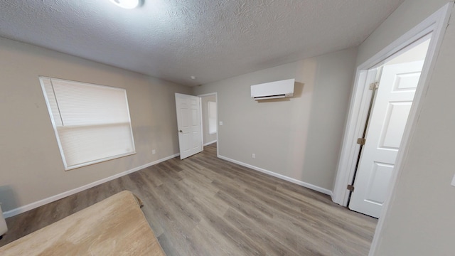 spare room with light hardwood / wood-style flooring, a wall unit AC, and a textured ceiling