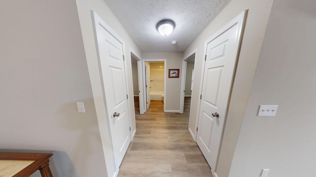 hall with light wood-type flooring and a textured ceiling