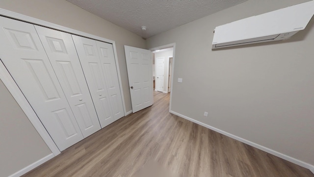 unfurnished bedroom featuring a closet, light wood-type flooring, a textured ceiling, and an AC wall unit