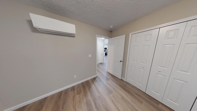 unfurnished bedroom featuring a wall mounted air conditioner, light hardwood / wood-style flooring, and a textured ceiling