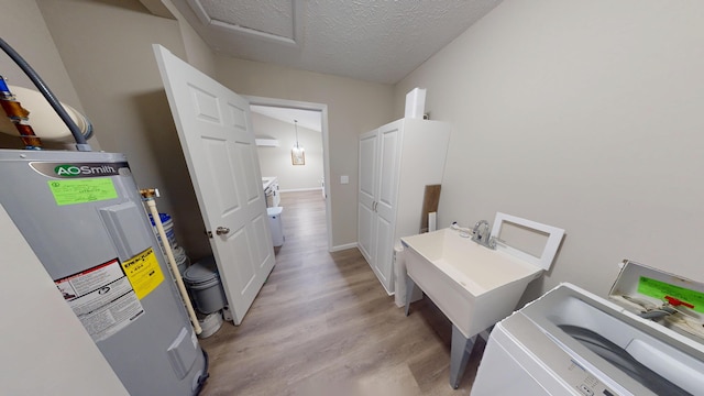 clothes washing area featuring electric water heater, light hardwood / wood-style flooring, and a textured ceiling