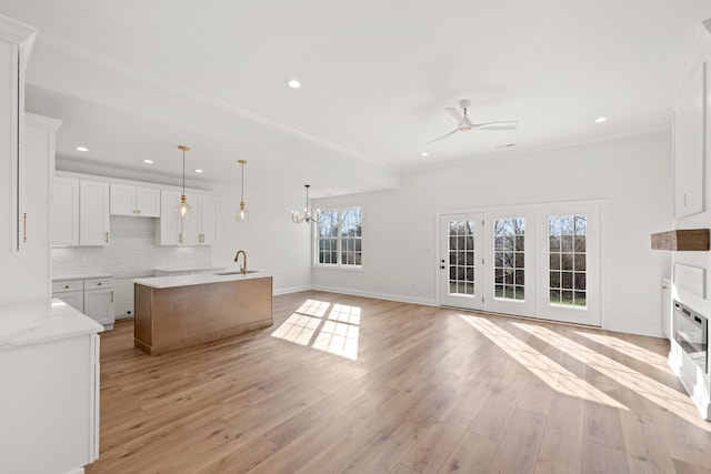 kitchen featuring pendant lighting, tasteful backsplash, white cabinetry, an island with sink, and light hardwood / wood-style flooring