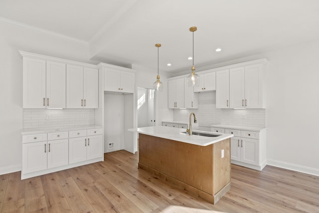 kitchen featuring a kitchen island with sink, sink, white cabinets, and decorative light fixtures