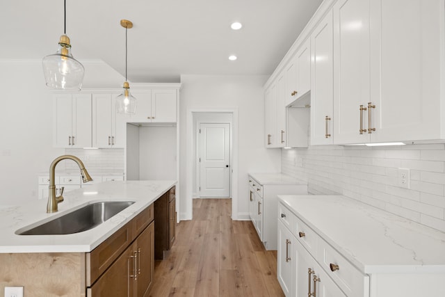 kitchen featuring white cabinetry, sink, pendant lighting, and light stone countertops