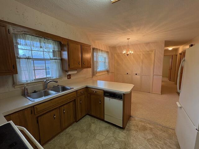 kitchen featuring sink, white appliances, a healthy amount of sunlight, decorative light fixtures, and kitchen peninsula