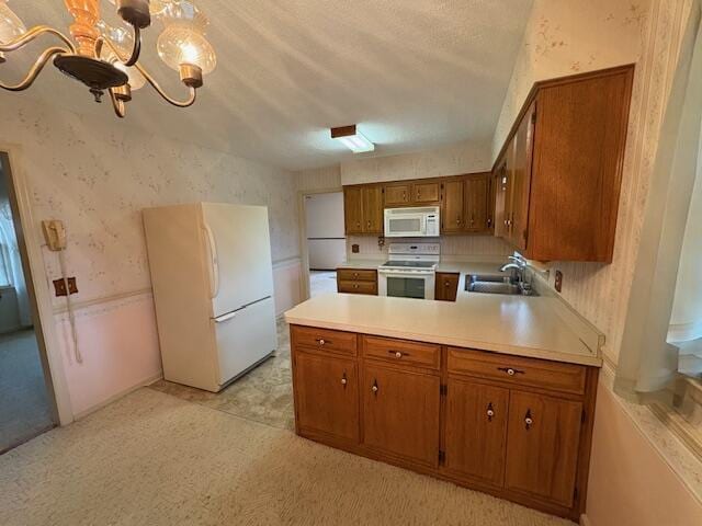 kitchen featuring sink, white appliances, an inviting chandelier, decorative light fixtures, and kitchen peninsula