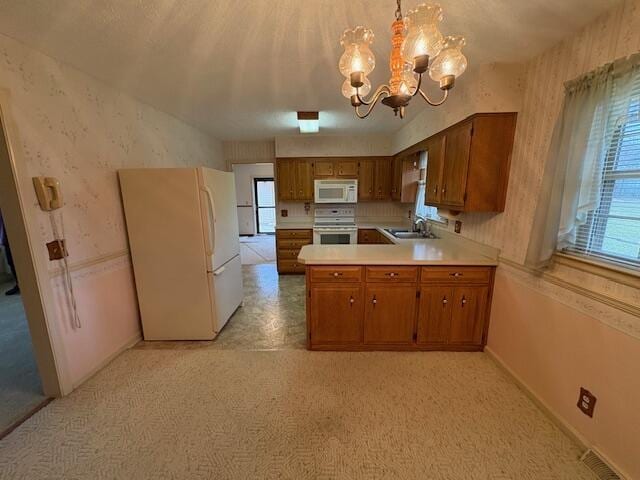 kitchen with sink, hanging light fixtures, white appliances, kitchen peninsula, and an inviting chandelier