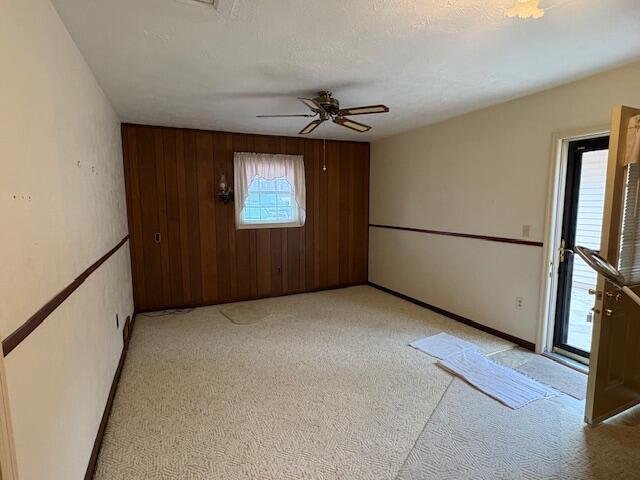 carpeted empty room featuring ceiling fan, a textured ceiling, and wood walls