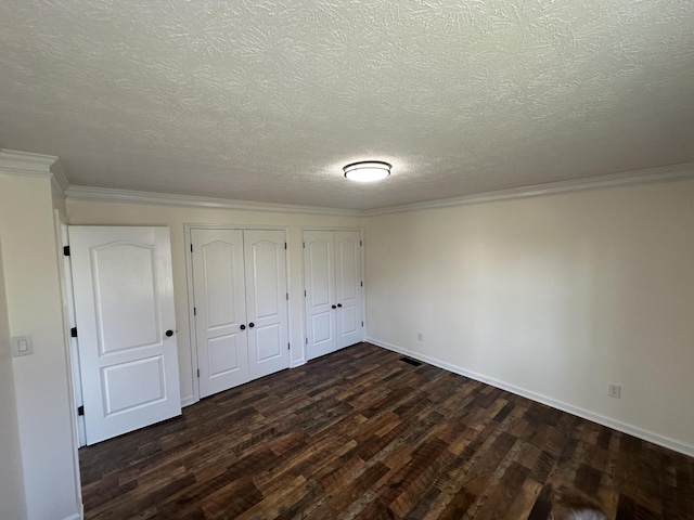 unfurnished bedroom with a textured ceiling, dark wood-type flooring, ornamental molding, and multiple closets