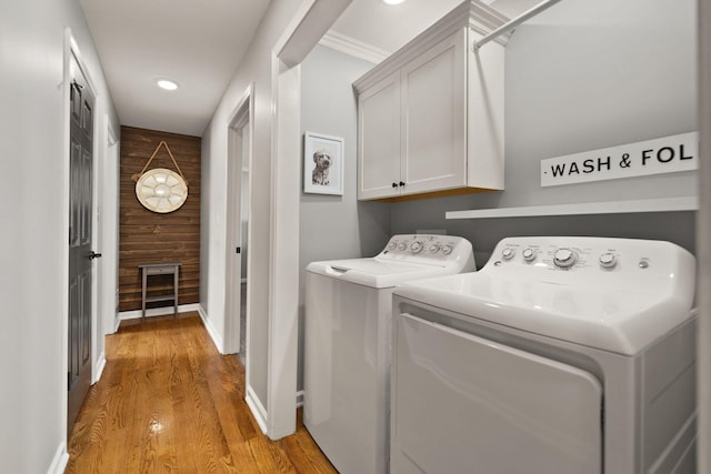 laundry area featuring cabinets, light hardwood / wood-style floors, washing machine and dryer, and wood walls