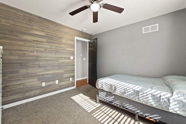 carpeted bedroom featuring ceiling fan and wood walls