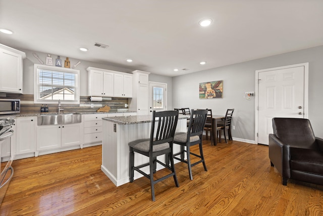 kitchen with stone counters, white cabinetry, sink, a kitchen bar, and a center island