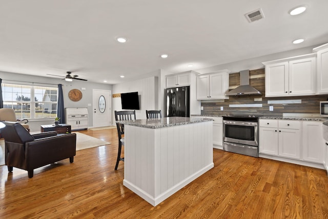 kitchen with white cabinetry, light stone counters, stainless steel appliances, and wall chimney exhaust hood