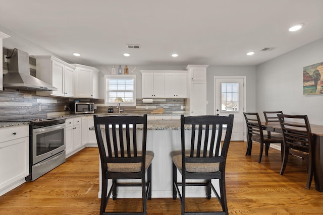 kitchen featuring white cabinets, light stone countertops, wall chimney exhaust hood, and appliances with stainless steel finishes