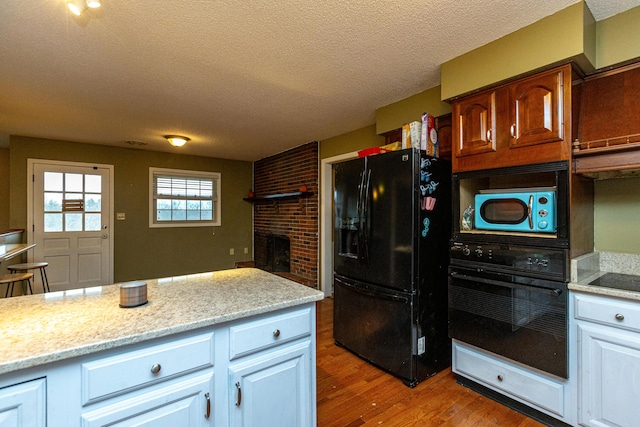 kitchen featuring a brick fireplace, white cabinetry, a textured ceiling, wood finished floors, and black appliances