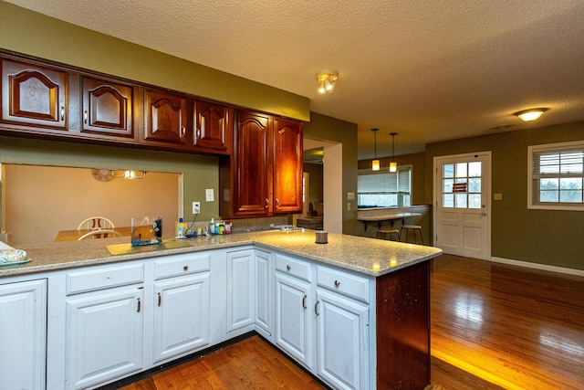 kitchen with light stone counters, pendant lighting, dark wood-type flooring, a textured ceiling, and a peninsula