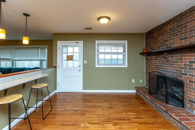 interior space with a textured ceiling, wood finished floors, visible vents, baseboards, and a brick fireplace