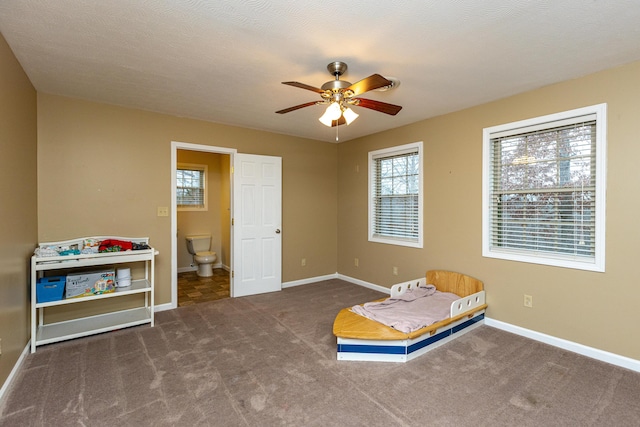 interior space featuring carpet floors, ensuite bath, baseboards, and a ceiling fan