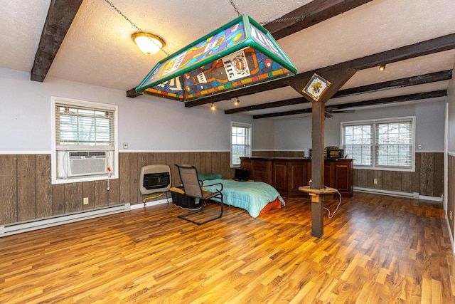 bedroom with a textured ceiling, a baseboard radiator, wood finished floors, wainscoting, and beam ceiling