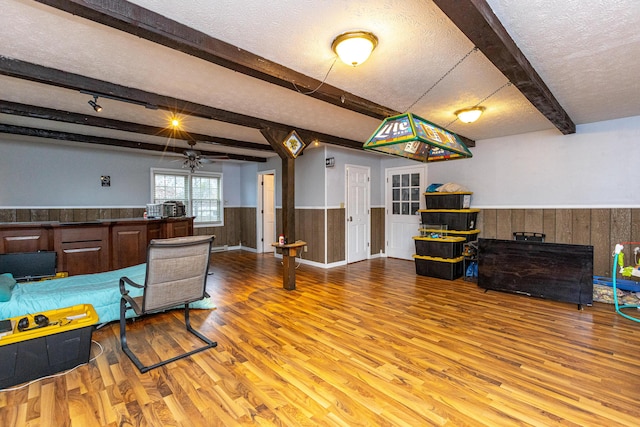 living room featuring a wainscoted wall, beamed ceiling, a textured ceiling, wood walls, and light wood-style floors