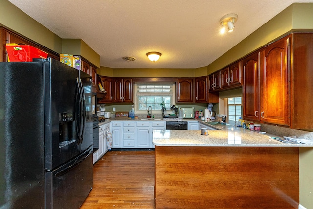 kitchen with light stone counters, a sink, wood finished floors, a peninsula, and black appliances